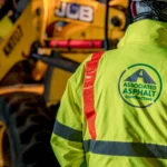 Close up of AA employee in branded PPE with digger in the back ground