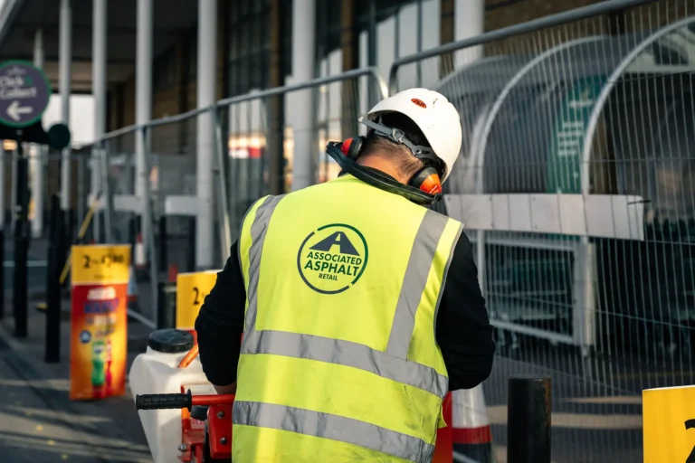 AA employee facing away standing near Heras fencing with full PPE in showing the Associated Asphalt Retail logo on the back of PPE